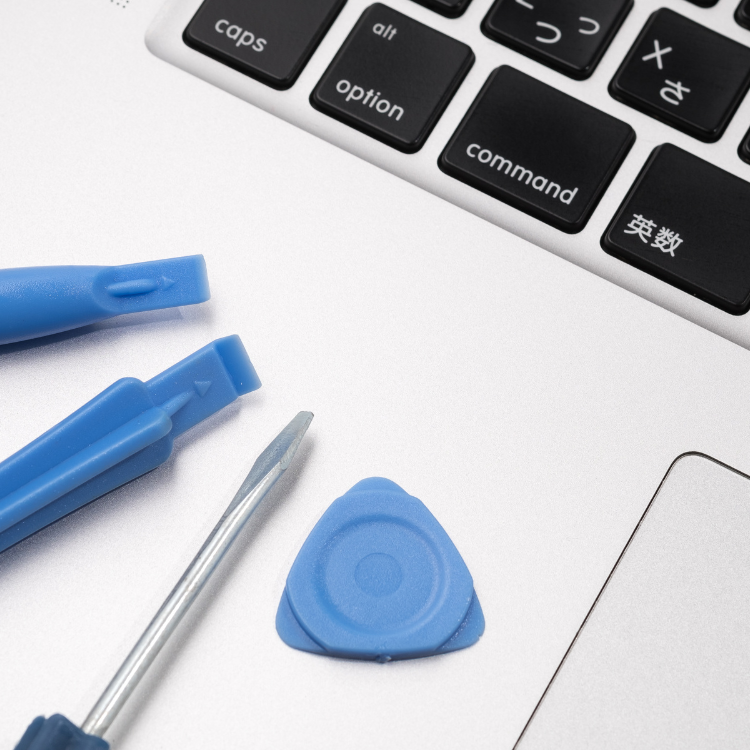 Professional laptop repair tools including blue plastic prying tools, precision screwdriver and triangular opening tool next to white laptop keyboard and trackpad